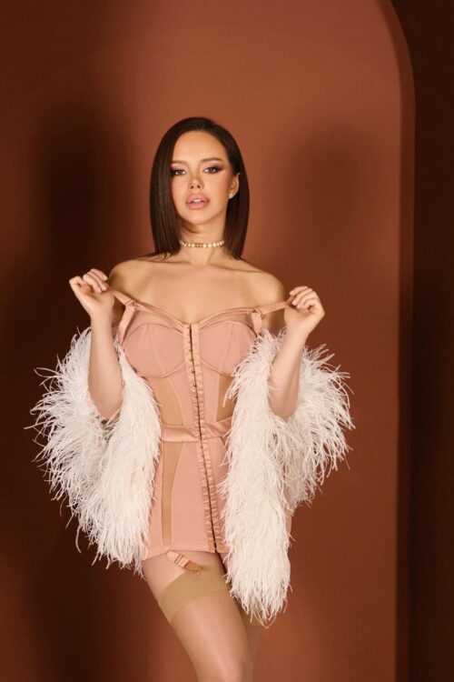 Woman in peach corset dress and white feather shawl.