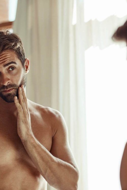 Man examining face in front of a mirror.