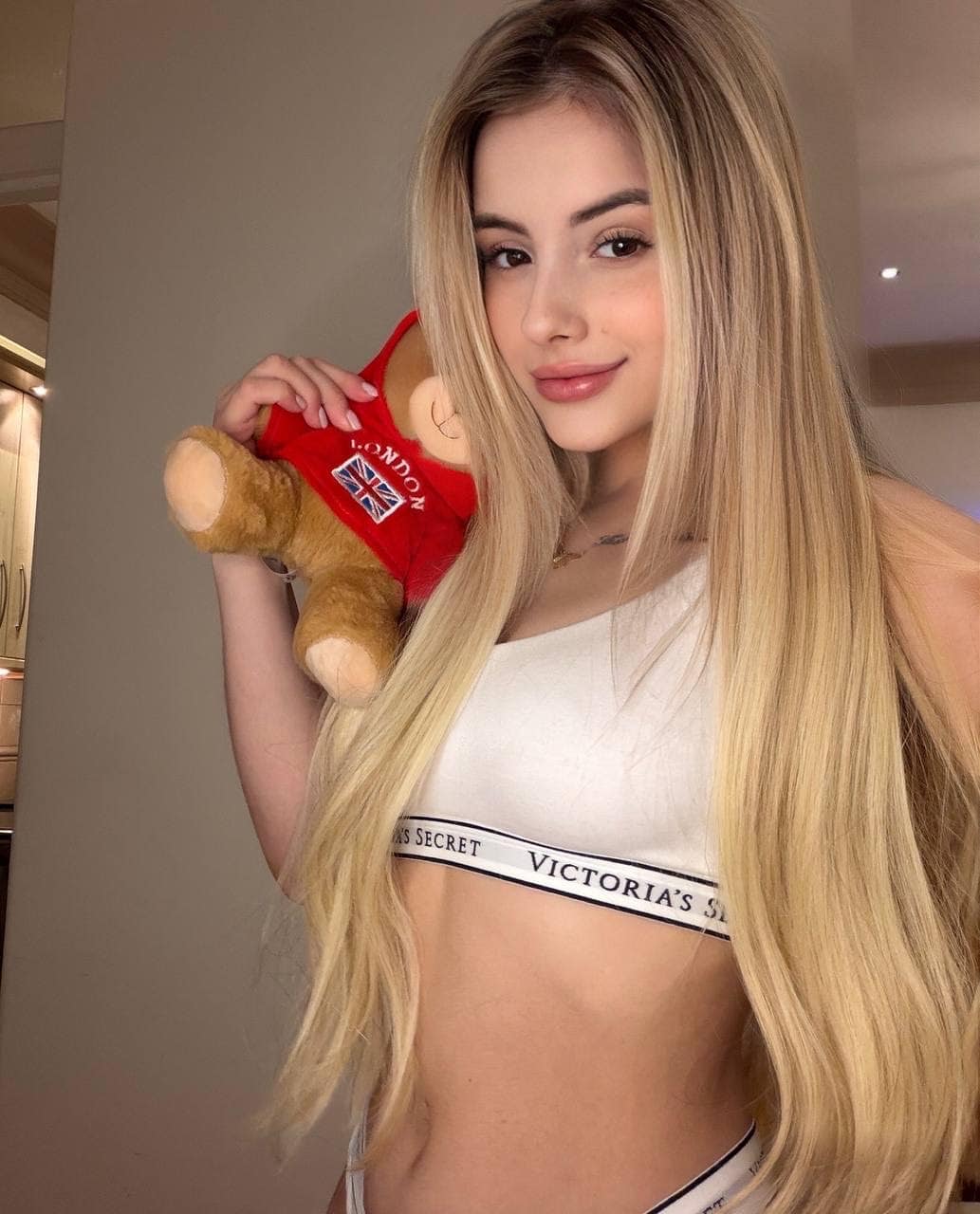 billa Blonde woman holding a London teddy bear in a white top.