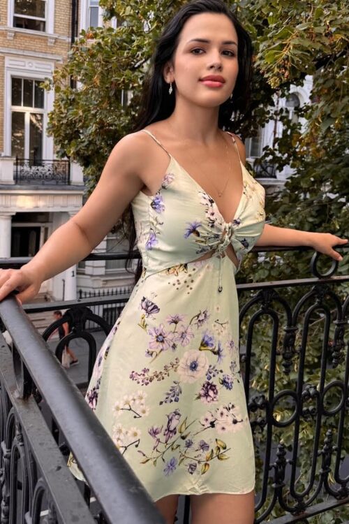Woman in a floral dress posing on a balcony.