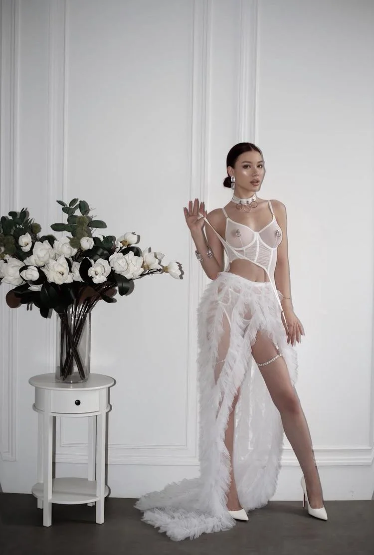 Woman posing in a sheer white outfit beside white flowers